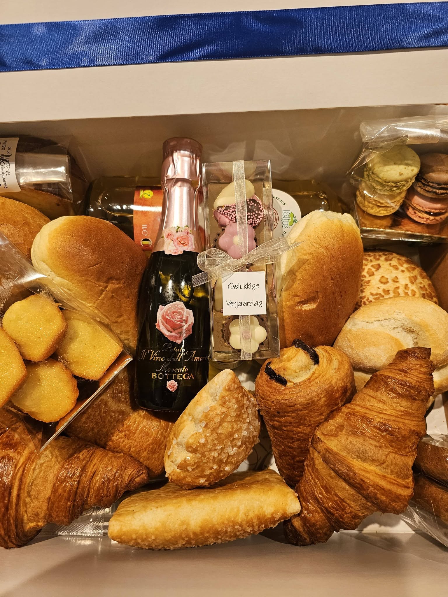 Geschenkmand met croissants, chocoladebroodjes, madeleines, macarons, pralines en een flesje bubbels