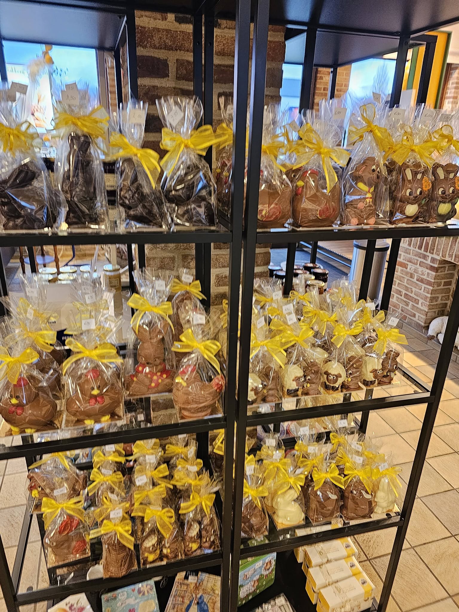 Rekken in de winkel vol paaschocolade: haasjes, kippen en lammetjes, elk ingepakt met een geel lint